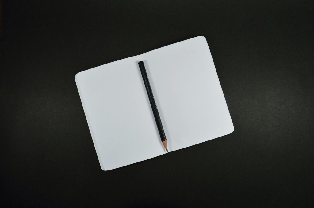 Top view of an open blank notebook with a pencil on a black background, perfect for creative projects.