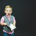 boy wearing gray vest and pink dress shirt holding book